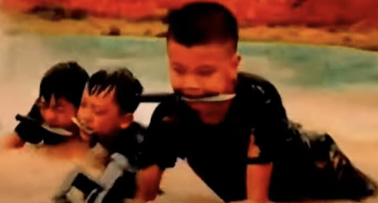 中国广西小学生军训让孩子们嘴含匕首在泥浆中匍匐前进。（视频截图）