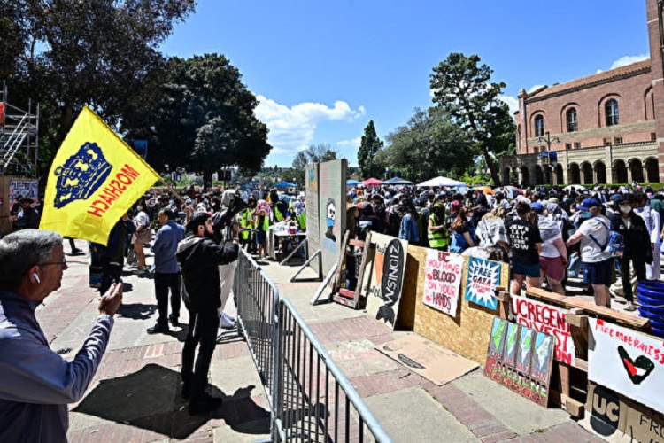 2024年4月26日，加州大学洛杉矶分校（UCLA）校园内，一名亲以色列支持者对着反犹示威者的营地挥舞旗帜。